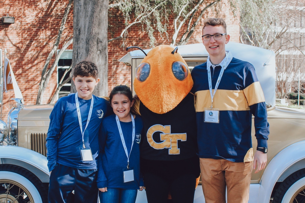 three smiling people with their arms around eachother and the Georgia Tech yellow jacket mascot, Buzz