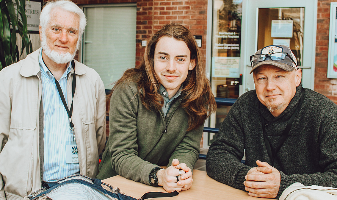 Caucasian grandfather, red-haired grandson, and father smiling at the camera.