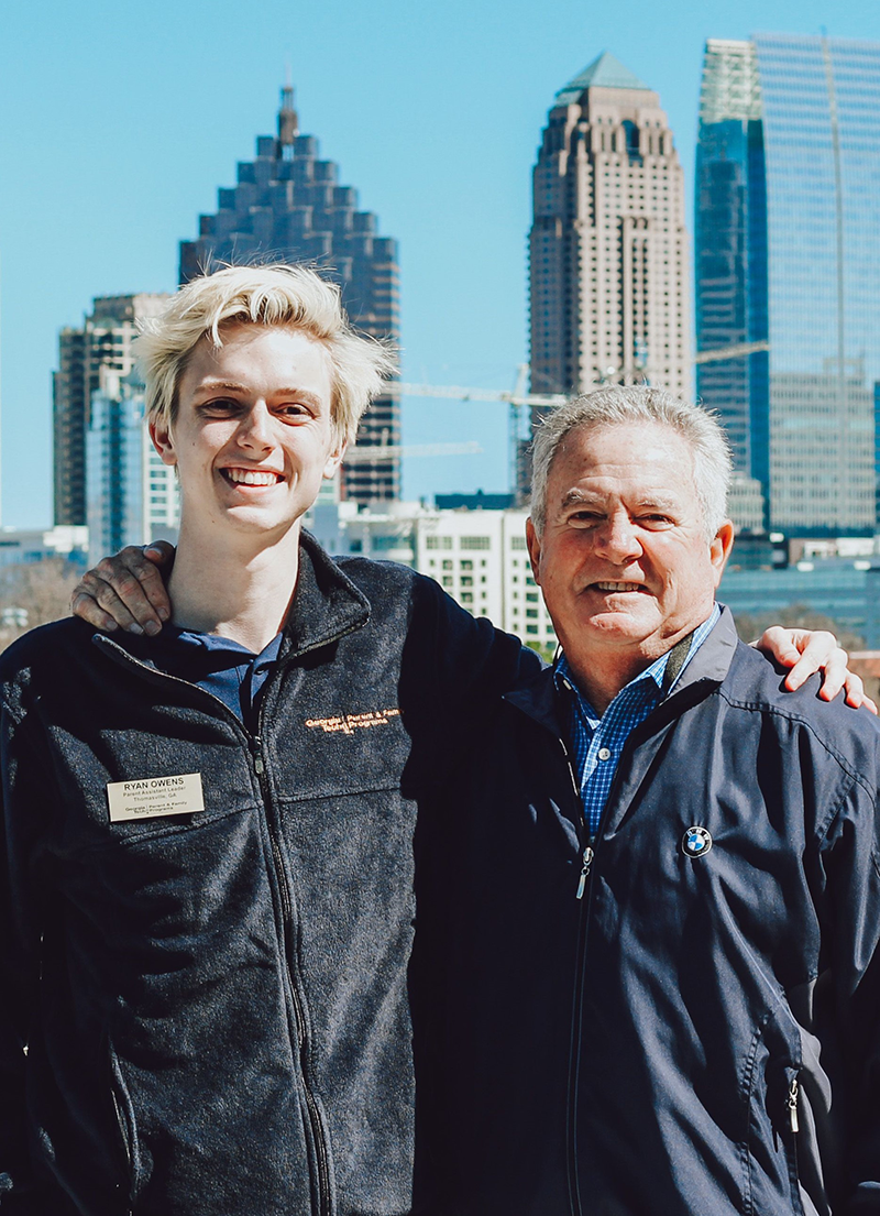 Smiling grandson and granpa with the Atlanta skyline as a brackdrop.