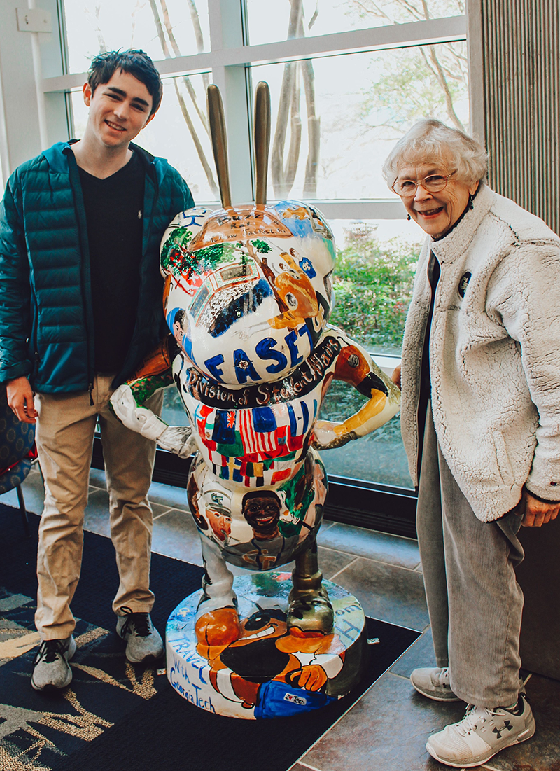 Smiling grandson and grandmother stating beside a sculpture of Buzz.