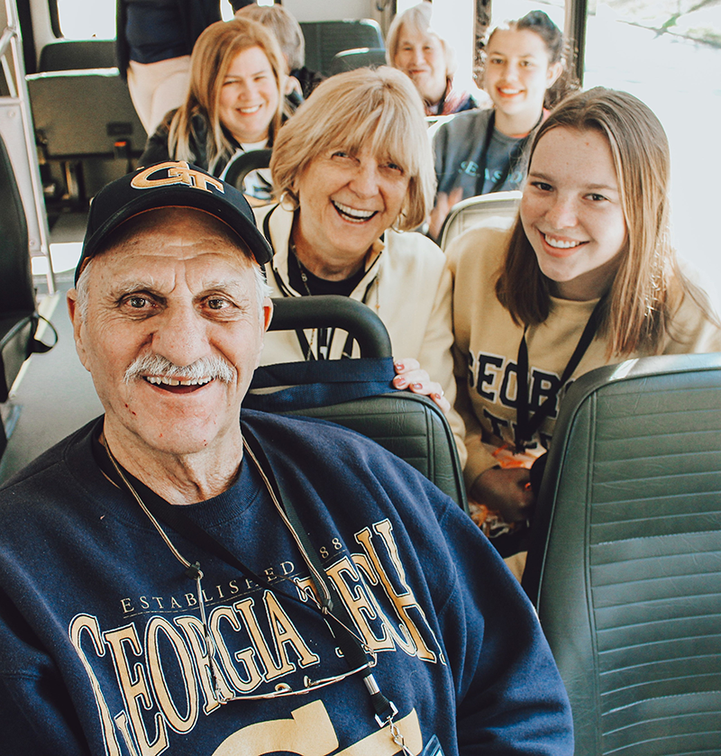 Smiling grandpa, grandma and granddaughter sitting on a bus.