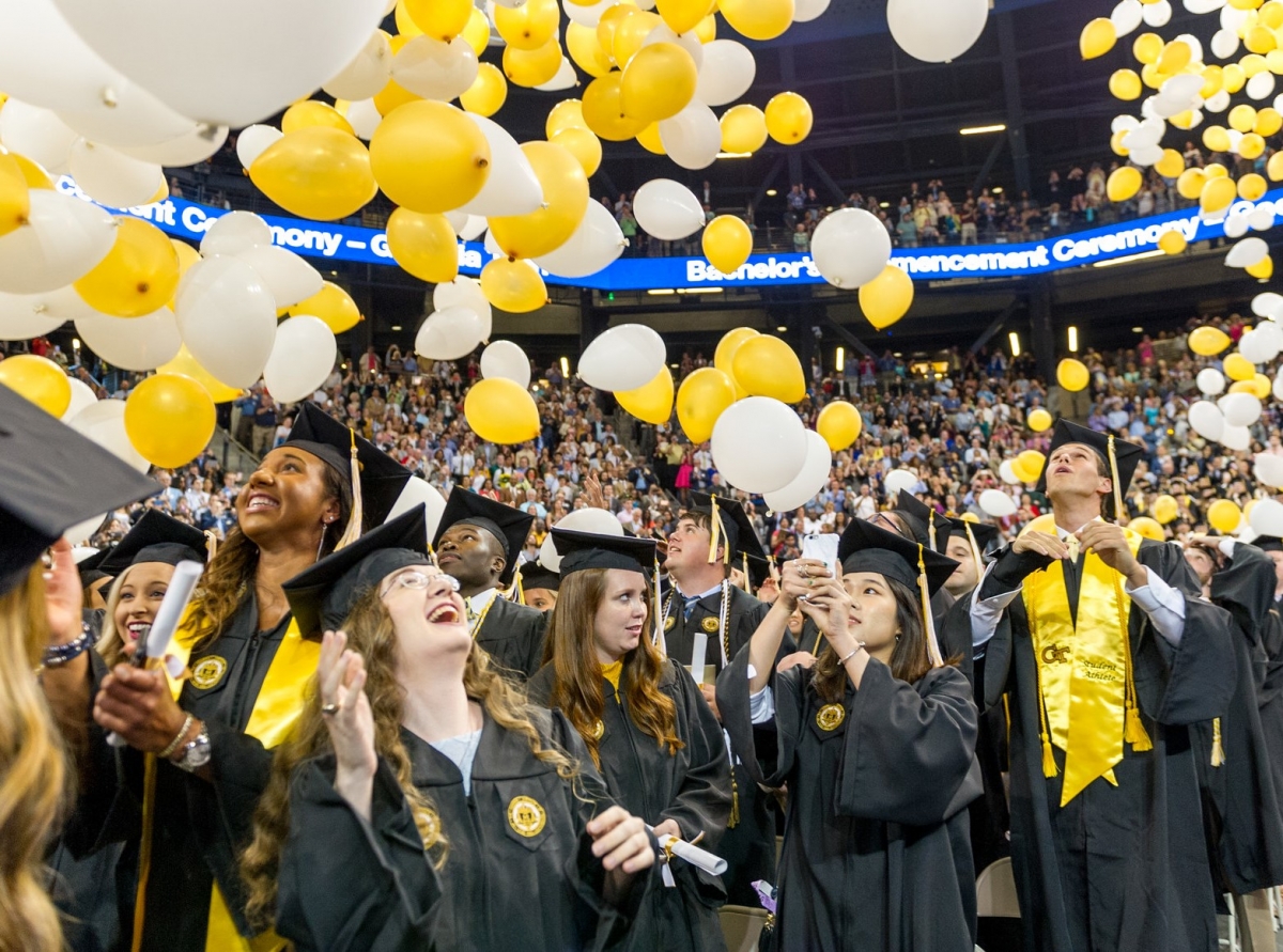  A group of graduates wearing their caps and gowns with floating yellow and white balloons.