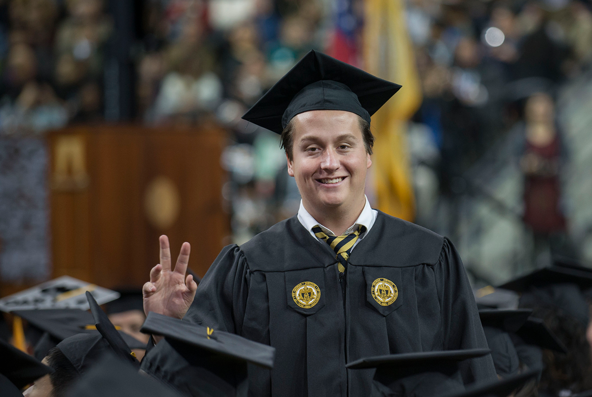 Male graduate wearing cap and gown smiling at the camera during the commencement ceremony.