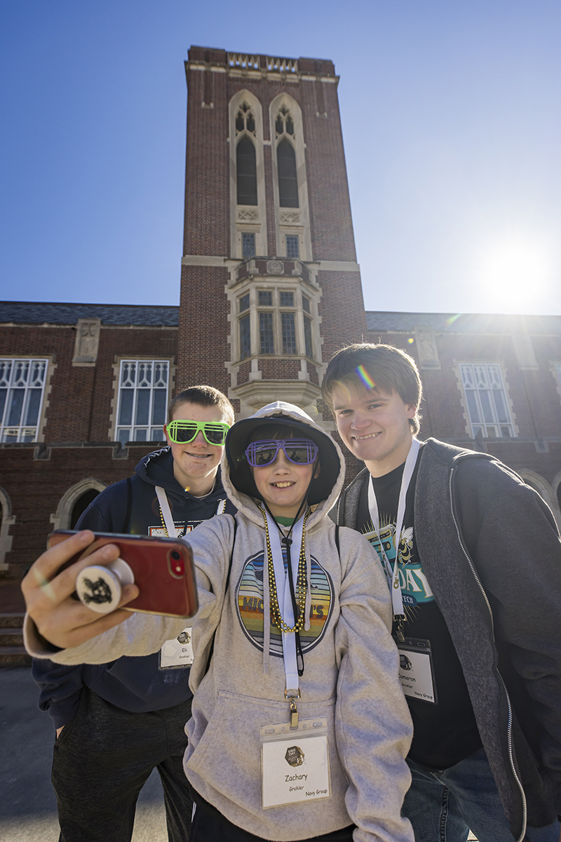 Three young men take a selfie in front of an ornate brick building