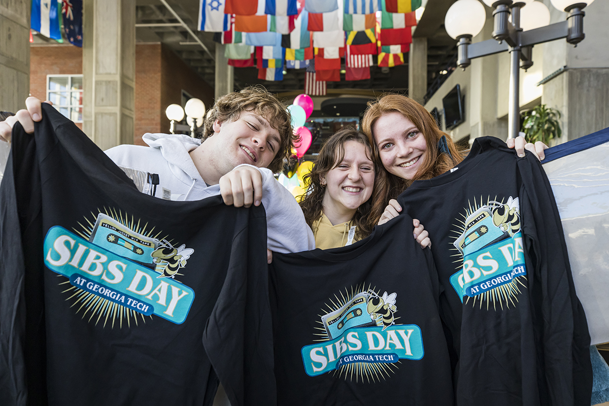 three smiling young people hold up T shirts that read Sibs Day at Georgia Tech