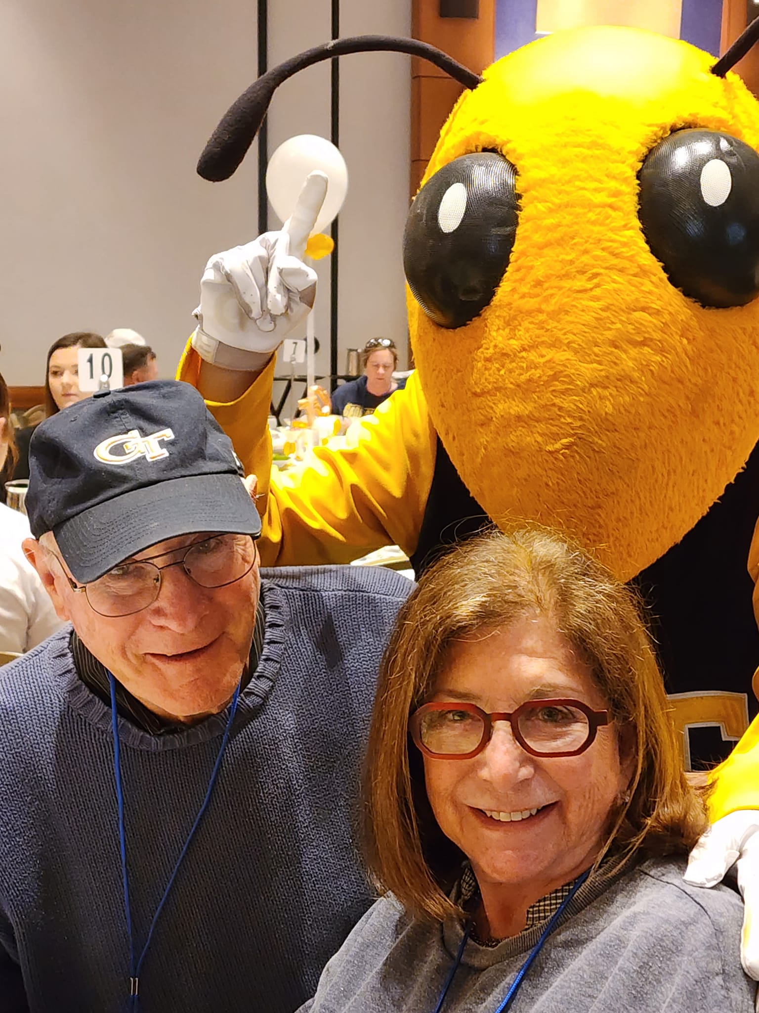 Grandpa is wearing a Georgia Tech baseball cap, sitting with grandma, and Buzz the yellow jacket stands behind them