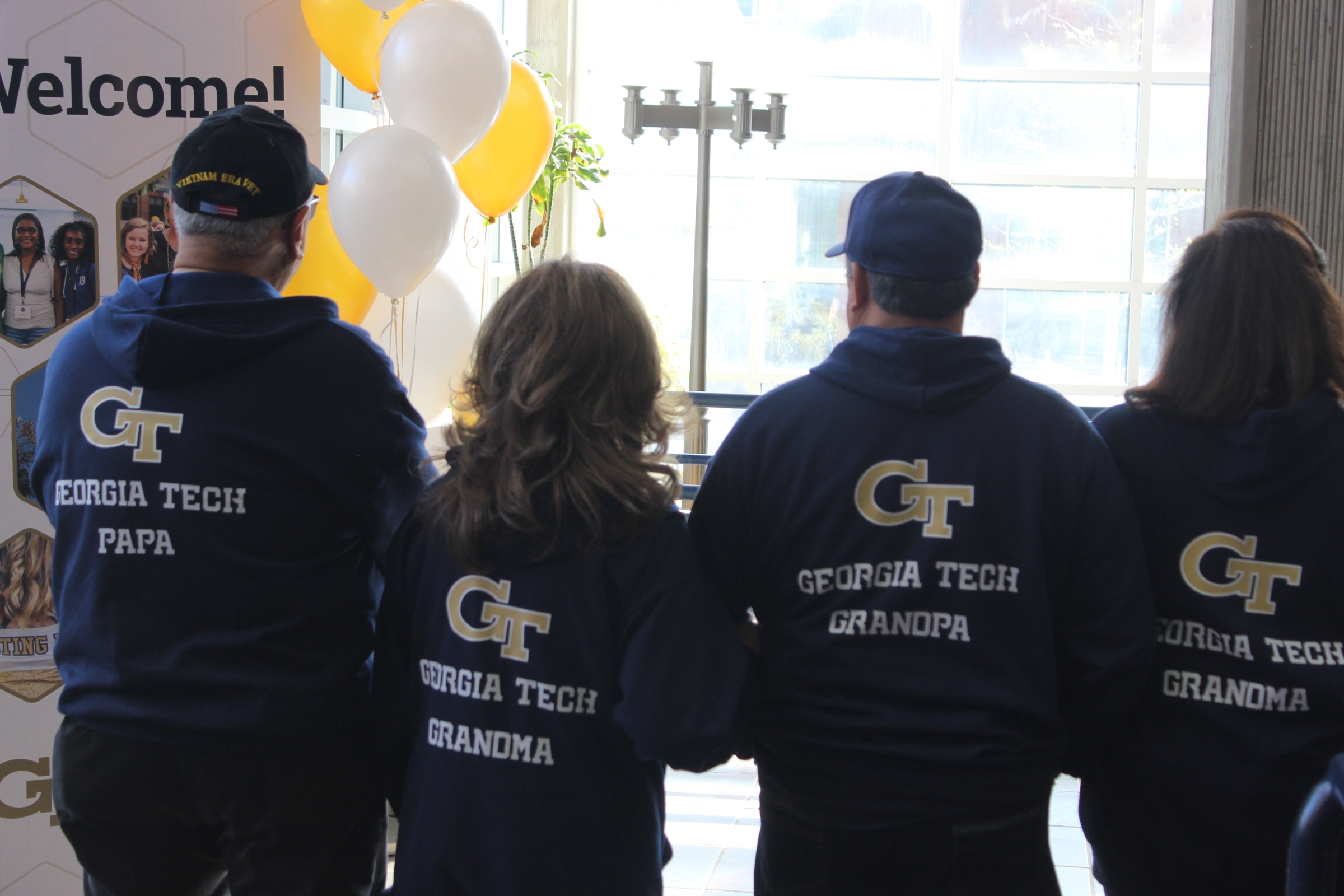 Four people stand with their backs to the camera, their shirts say GT Grandpa, Grandma, and Papa