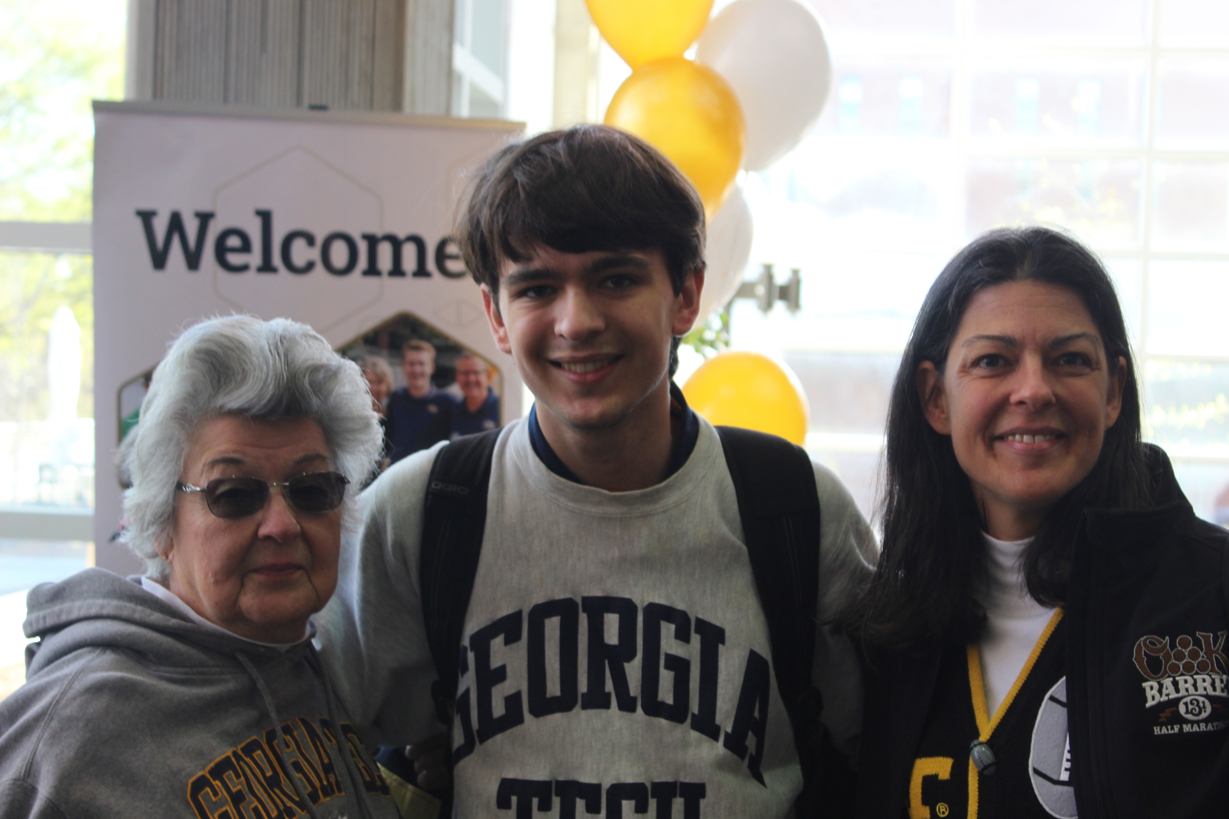 A woman with short grey hair stands next to a young man wearing a Georgia Tech sweatshirt, next to whom is a woman with dark hair.