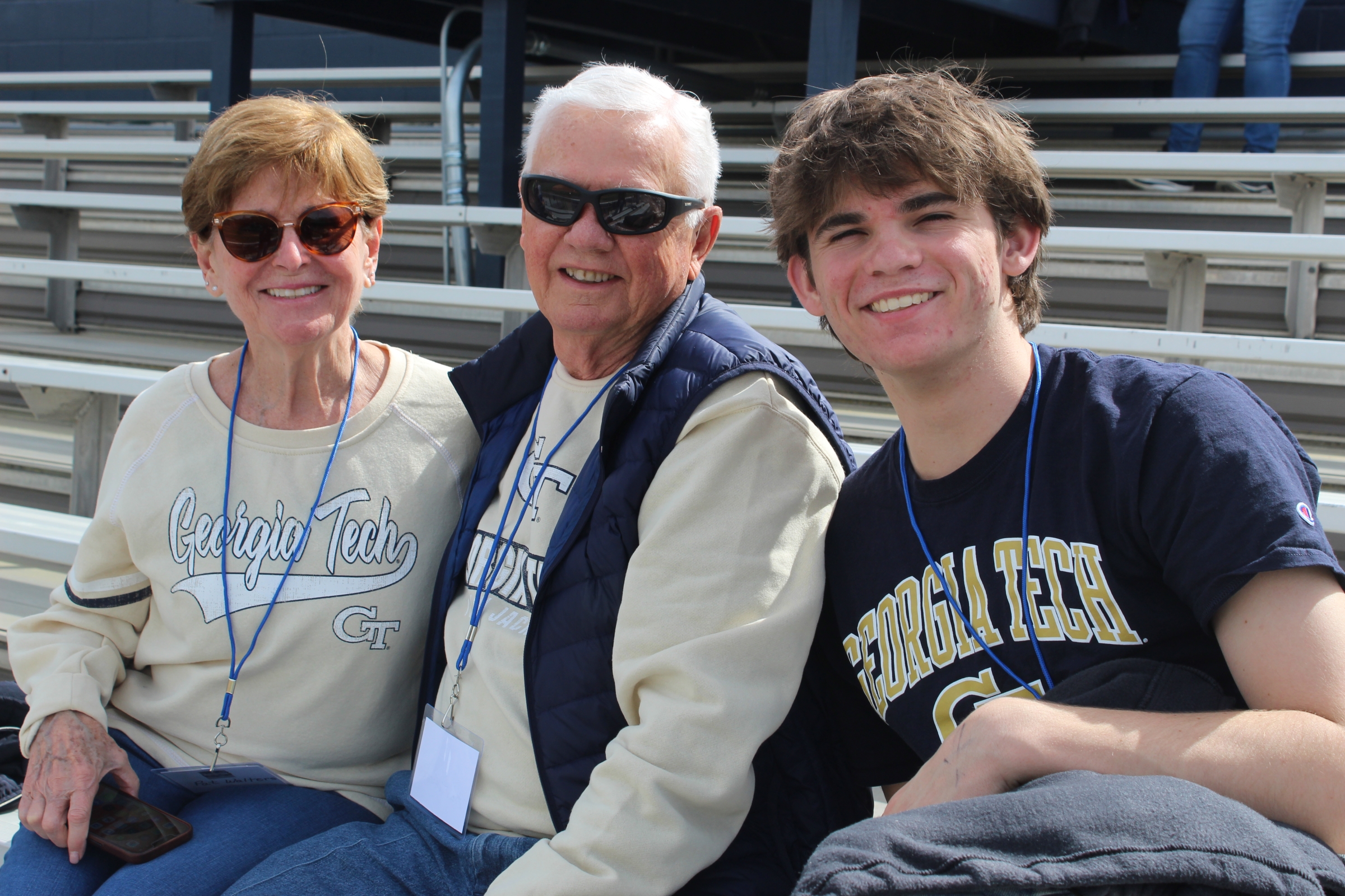 In a baseball stadium a man and woman sit next to their college-age grandson