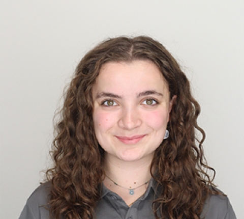 a young white woman with brown curly hair to just below her shoulders smiles at the camera