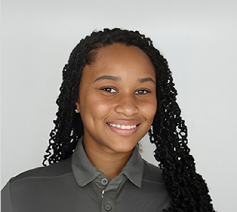 A young Black woman with long hair smiles at the camera